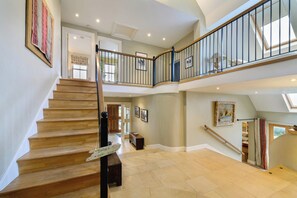 Un intérieur spacieux avec un escalier en bois, un balcon au deuxième étage et une vue sur l’extérieur.