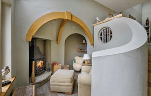 Un salon chaleureux avec une cheminée en pierre, un mur blanc incurvé et une arche en bois.