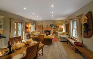 Ein gemütliches Wohnzimmer mit Kamin, Holzmöbeln und einem Essbereich mit einem stimmungsvollen Tisch.