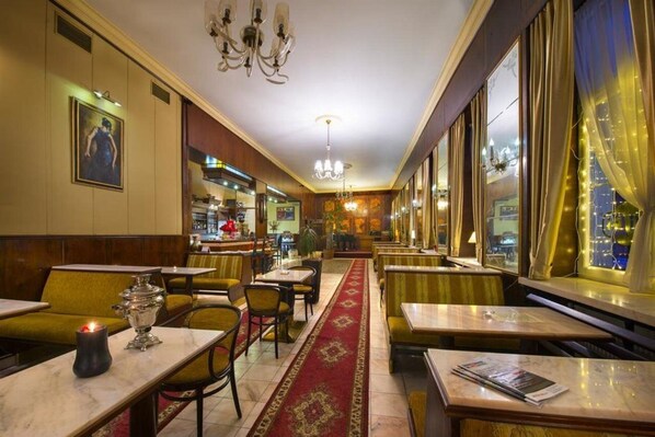 A restaurant with booths and tables, a chandelier, and a city view through large windows. - Hotel Europa Poprad (Poprad)