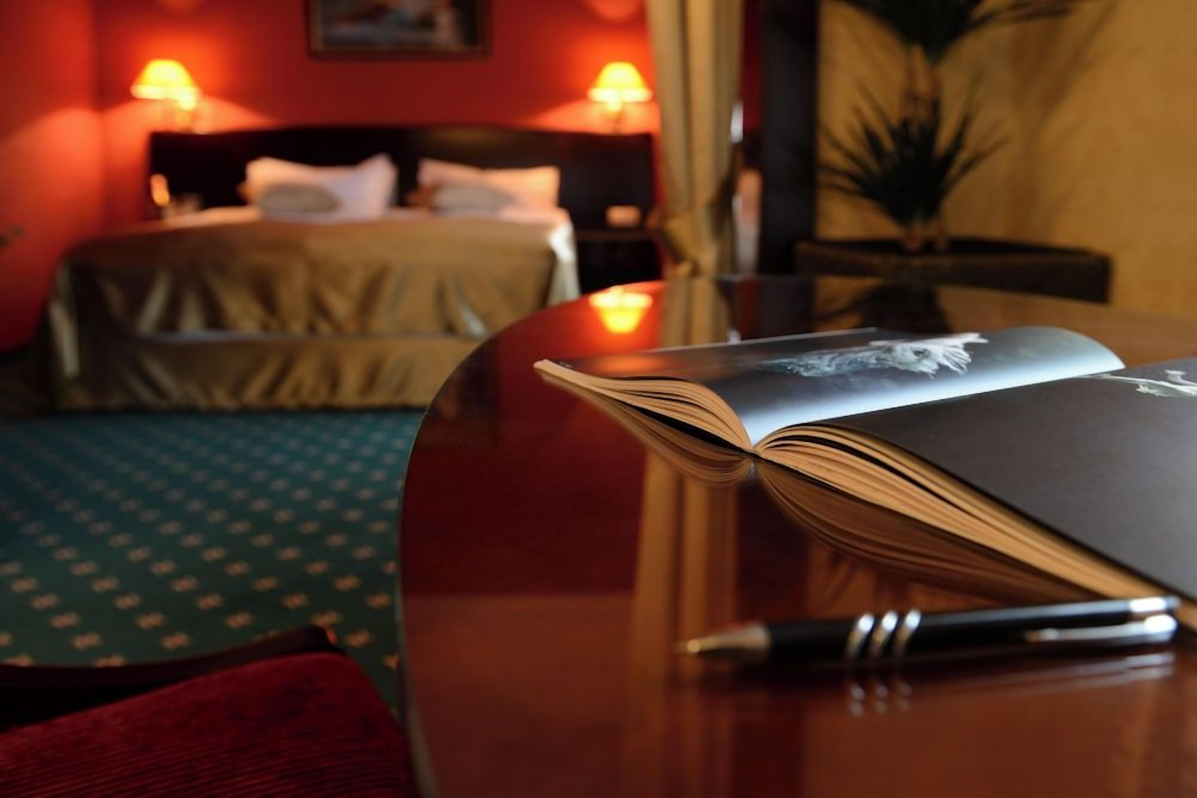 Ein Hotelzimmer mit einem Bett, einem Nachttisch mit Buch und Stift sowie einer Lampe.