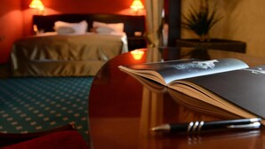 Quarto de hotel com uma cama, uma mesa de cabeceira com um livro e uma caneta, e duas luminárias de cada lado da cama.