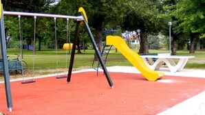 A playground with swings and a slide, surrounded by trees and a picnic table. - -- Diligence -- (Aire-sur-l'Adour)