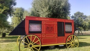 A red and yellow U.S. Mail cart with "West Air City" and "VK Company" branding, parked on grass with trees in the background. - -- Diligence -- (Aire-sur-l'Adour)