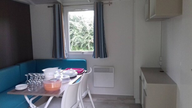 Ein gemütlicher Raum mit Küchenzeile, einem Esstisch mit Stühlen, einem blauen Sofa und einem Fenster mit Vorhängen.