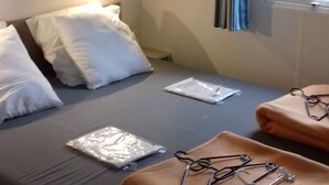 Ein Einzelbett mit weißen Kissen, ein Nachttisch mit einer Lampe und ein Fenster mit Vorhängen.