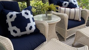 A wicker lounge area with two sofas and a small table, featuring a stop sign and greenery in the background. - 2BR Naples Bay Resort Condo (Naples)