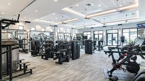 A modern gym with various exercise machines, mirrors, and a large window providing natural light. - 2BR Naples Bay Resort Condo (Naples)