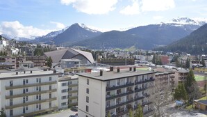 A multi-story building with balconies, a sports field, and a mountainous backdrop. - Spengler Hostel (Davos)