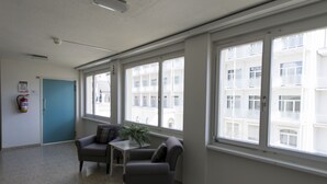 A room with large windows, a fire extinguisher, a door, and a small table with a plant. - Spengler Hostel (Davos)