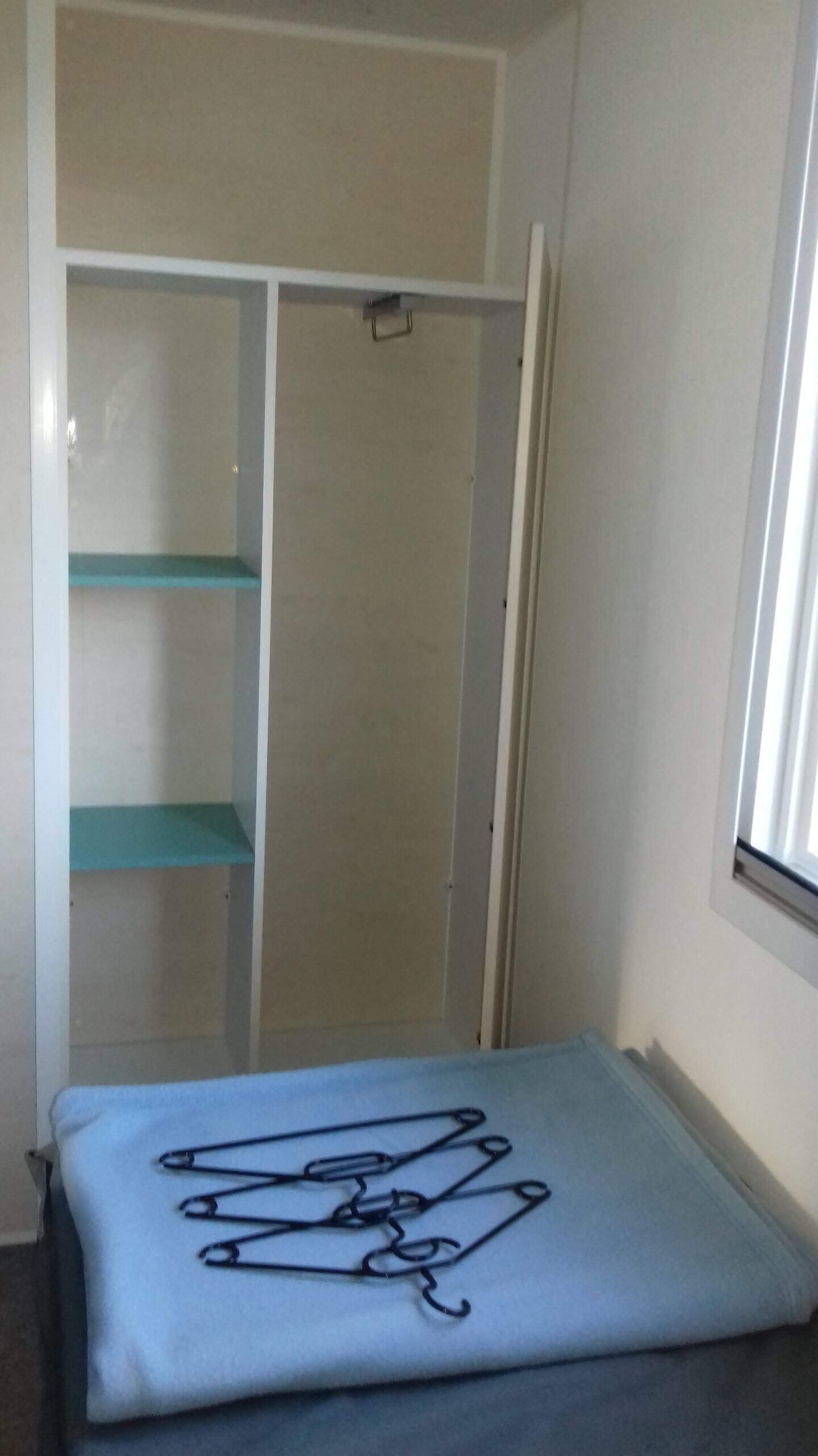 Une pièce comprenant un lit, une armoire blanche avec une étagère turquoise et une fenêtre.