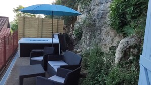 Un patio al aire libre con una mesa, sillas, un paraguas azul y un muro de piedra.