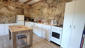 Una cocina compacta con armarios blancos, una mesa de madera y una pared de piedra.