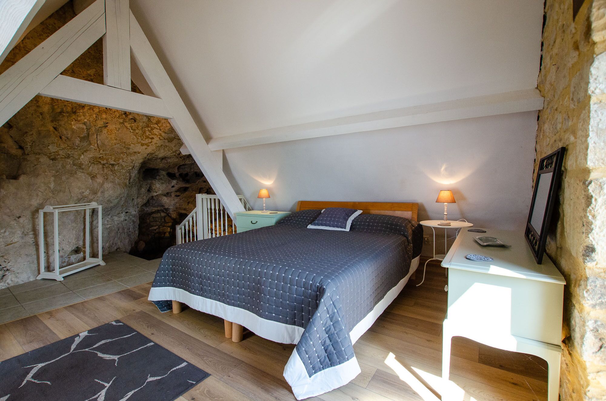 Een slaapkamer met een groot bed, een nachtkastje, een lamp, een stenen muur en een houten vloer.