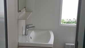 A bathroom with a white sink, mirror, and window. - Mobile home with large terrace 300m from the city (Aire-sur-l'Adour)
