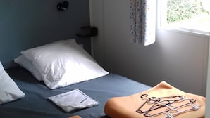 A small, single-bed room with a window, a curtain, and a bedside table with a lamp. - Mobile home with large terrace 300m from the city (Aire-sur-l'Adour)