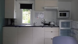 A compact kitchen with white cabinets, a window, a microwave, and a stove. - Mobile home with large terrace 300m from the city (Aire-sur-l'Adour)