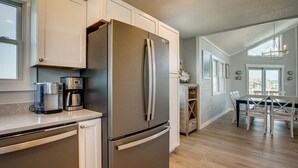 A modern kitchen with a stainless steel refrigerator, a coffee maker, and a dining area with a table and chairs. - Singing Sandpipers | 325 ft to the beach | Private Pool, Dog Friendly, Community Pool (Duck)