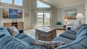 A spacious living room with a large sofa, a coffee table, and a view of the outside through a sliding glass door. - Singing Sandpipers | 325 ft to the beach | Private Pool, Dog Friendly, Community Pool (Duck)