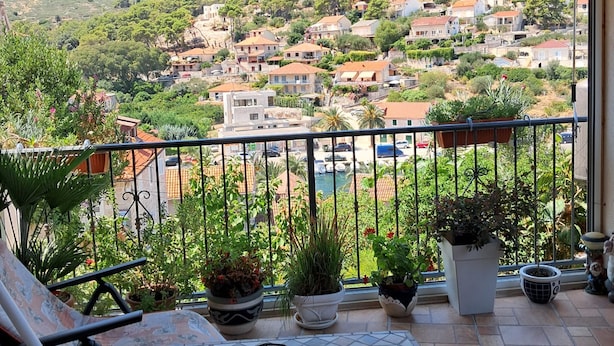 Un balcón con vistas a un pueblo en la ladera, plantas en macetas y un toldo a rayas.