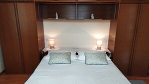 Una cama bien hecha con dos almohadas, dos lámparas de noche y una pequeña estatua en la mesita.