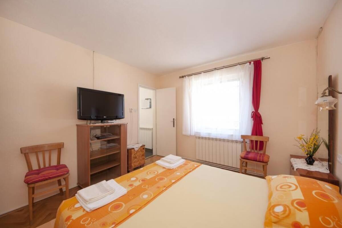 A hotel room with a bed, a television on a stand, a window with curtains, and a chair.