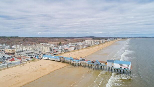 A coastal hotel with a pier extending into the ocean, featuring multiple buildings and a sandy beach.