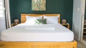 Un letto con struttura in legno, biancheria bianca e un cuscino verde. Sono presenti due comodini con lampade.