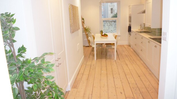 Een moderne keuken met witte kasten, een houten vloer en een eethoek met een tafel en stoelen.
