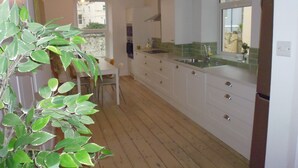 A modern kitchen with white cabinets, a wooden floor, and a large window. - Stunning townhouse at Plymouth Hoe (Plymouth)