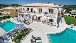 A large two-story house with a swimming pool, sun loungers, and a covered patio area.
