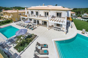 A large two-story house with a swimming pool, sun loungers, and a covered patio area.
