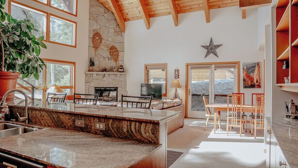 A spacious kitchen with granite countertops, a stone fireplace, and a dining area with wooden chairs.