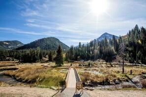 A wooden bridge leading to a mountainous area with dense forests and a clear sky. - Powderhorn Suite by Cottonwood Lodging (Solitude)