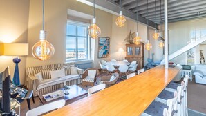 A spacious living area with a long wooden table, multiple seating options, and hanging light fixtures.