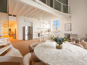 A modern interior with a marble dining table, white furniture, and a kitchen area with stainless steel appliances.