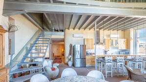 A spacious living area with a marble table, white chairs, a staircase, and a kitchen area with modern appliances.