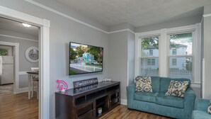 A living room with a teal sofa, a flat-screen TV mounted on the wall, and a wooden entertainment center. - Vibrant, Historical Escape in Phoebus! (Hampton)