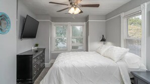 A bedroom with a bed, a ceiling fan, a dresser, a TV, and windows. - Vibrant, Historical Escape in Phoebus! (Hampton)
