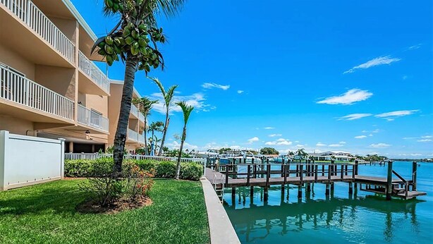 Een hotel aan het water met een steiger, palmbomen en een helderblauwe lucht.