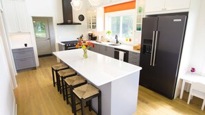 Una cocina moderna con una isla central, taburetes de bar, un refrigerador y un ventanal con vistas a la vegetación.