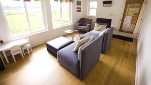 Una sala de estar moderna con un sofá, un sillón y una pequeña mesa. Hay ventanas amplias que dan a un campo verde.