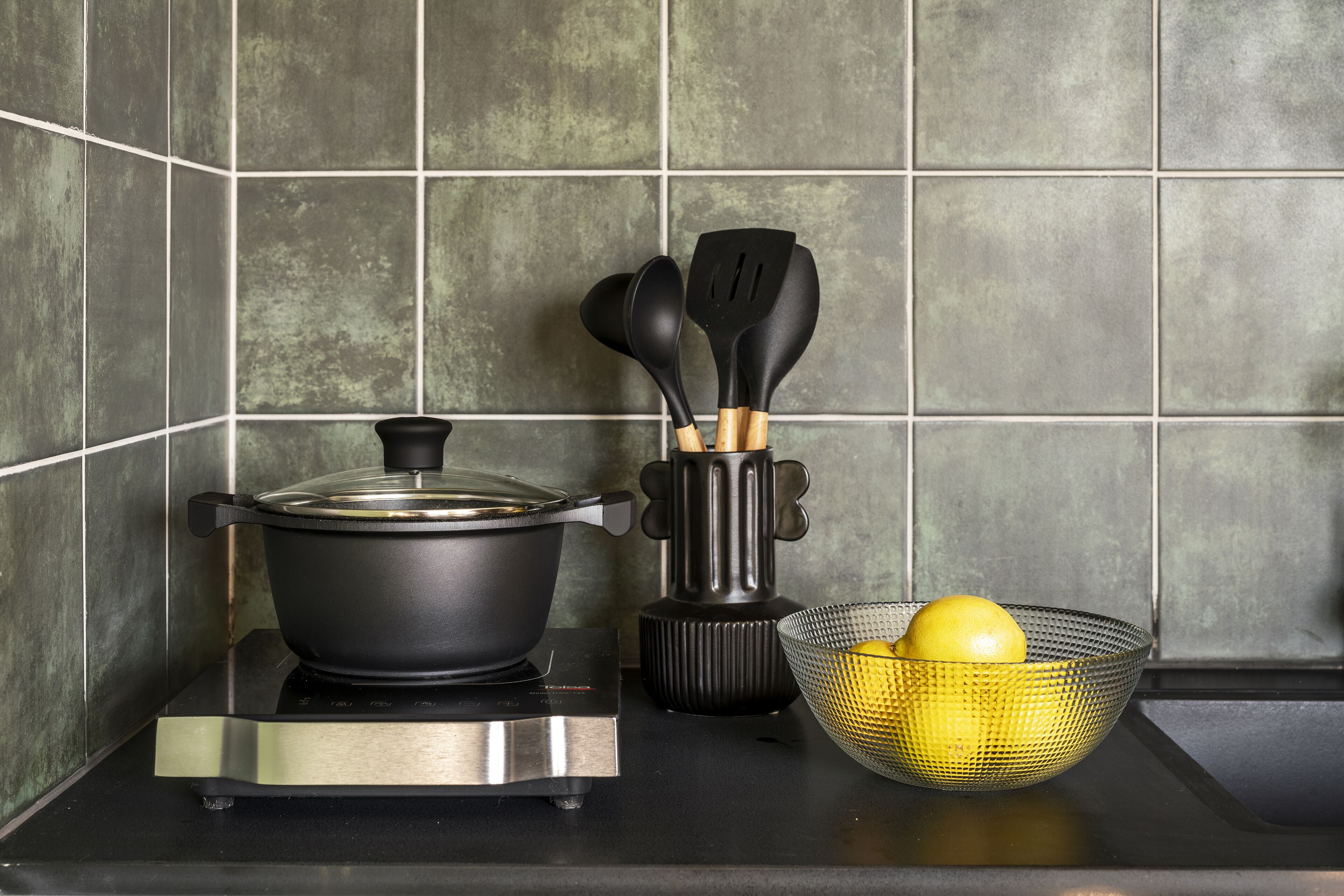 A kitchen with a stove, a pot, a colander with lemons, and a utensil holder.