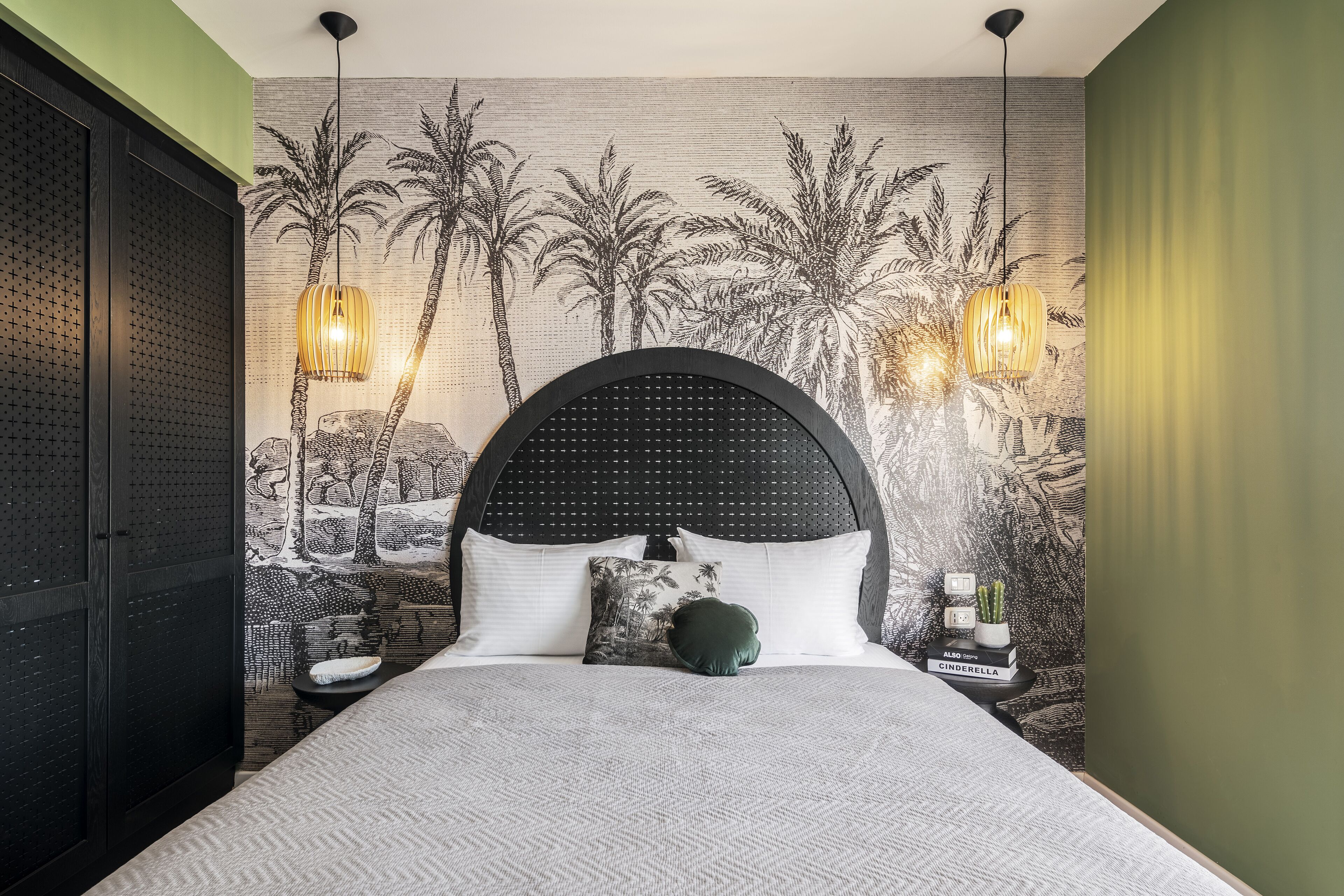 A bedroom with a large bed, a headboard with a circular pattern, two wall-mounted lamps, and a mural of palm trees.