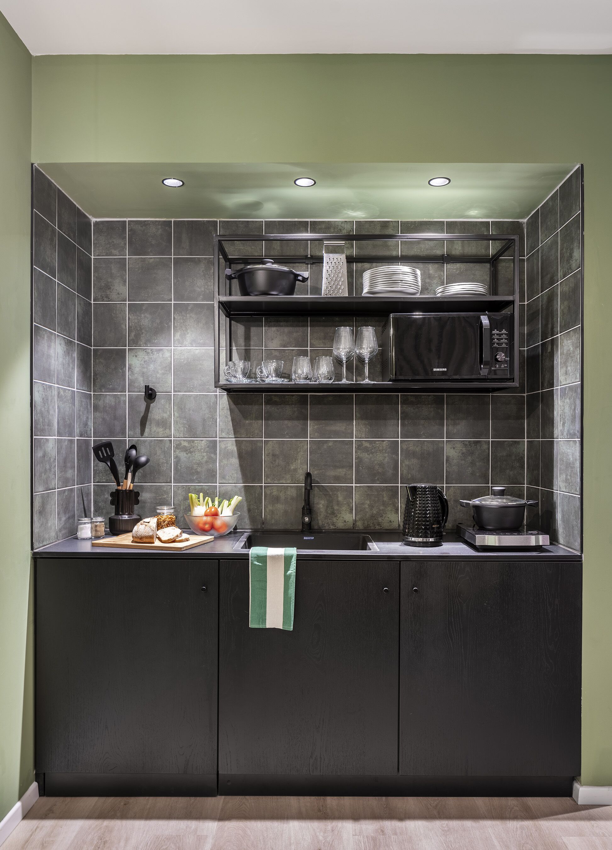 Een moderne keuken met donkere kastjes, een magnetron, een spoelbak en een aanrecht met verschillende keukenbenodigdheden.