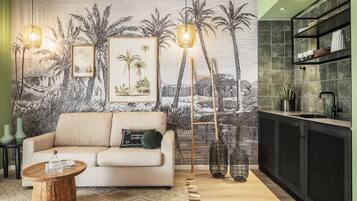 Una sala de estar con un sofá color beige, una mesa de centro de madera, un tapete estampado y un mural de palmeras en la pared.