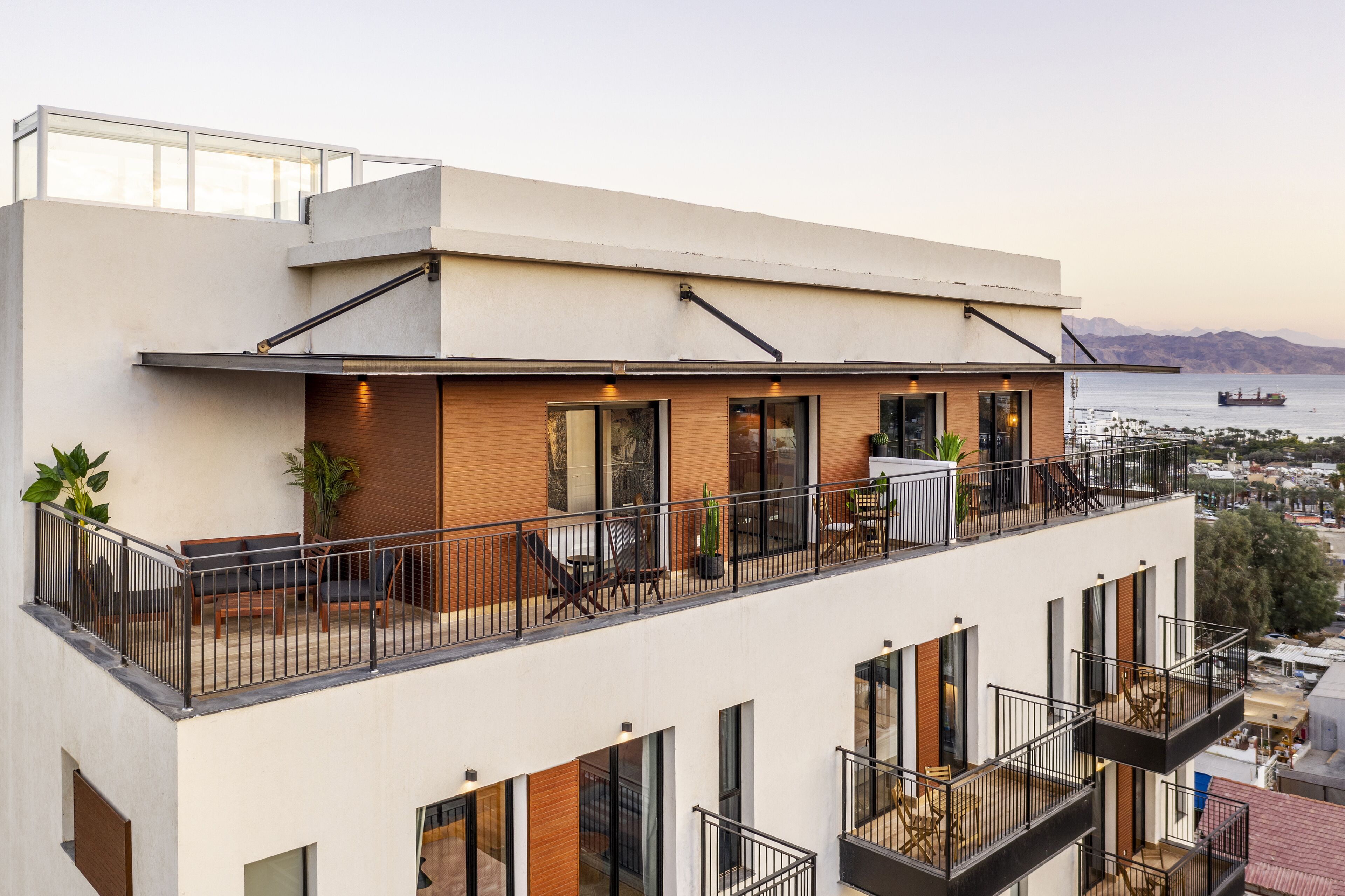 A modern building with multiple balconies, large windows, and a view of the sea.
