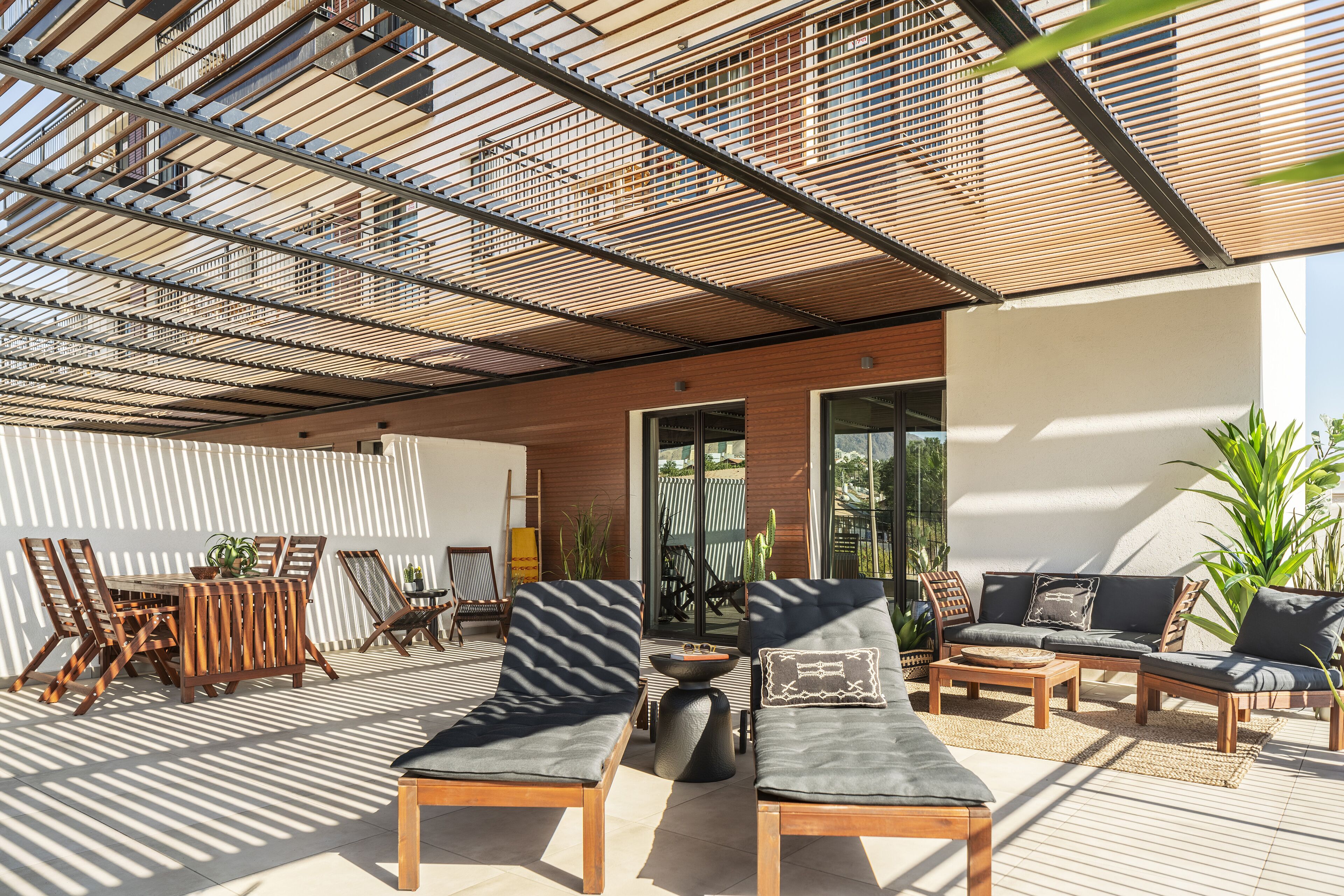 An outdoor patio with wooden furniture, including two lounge chairs and a dining table.