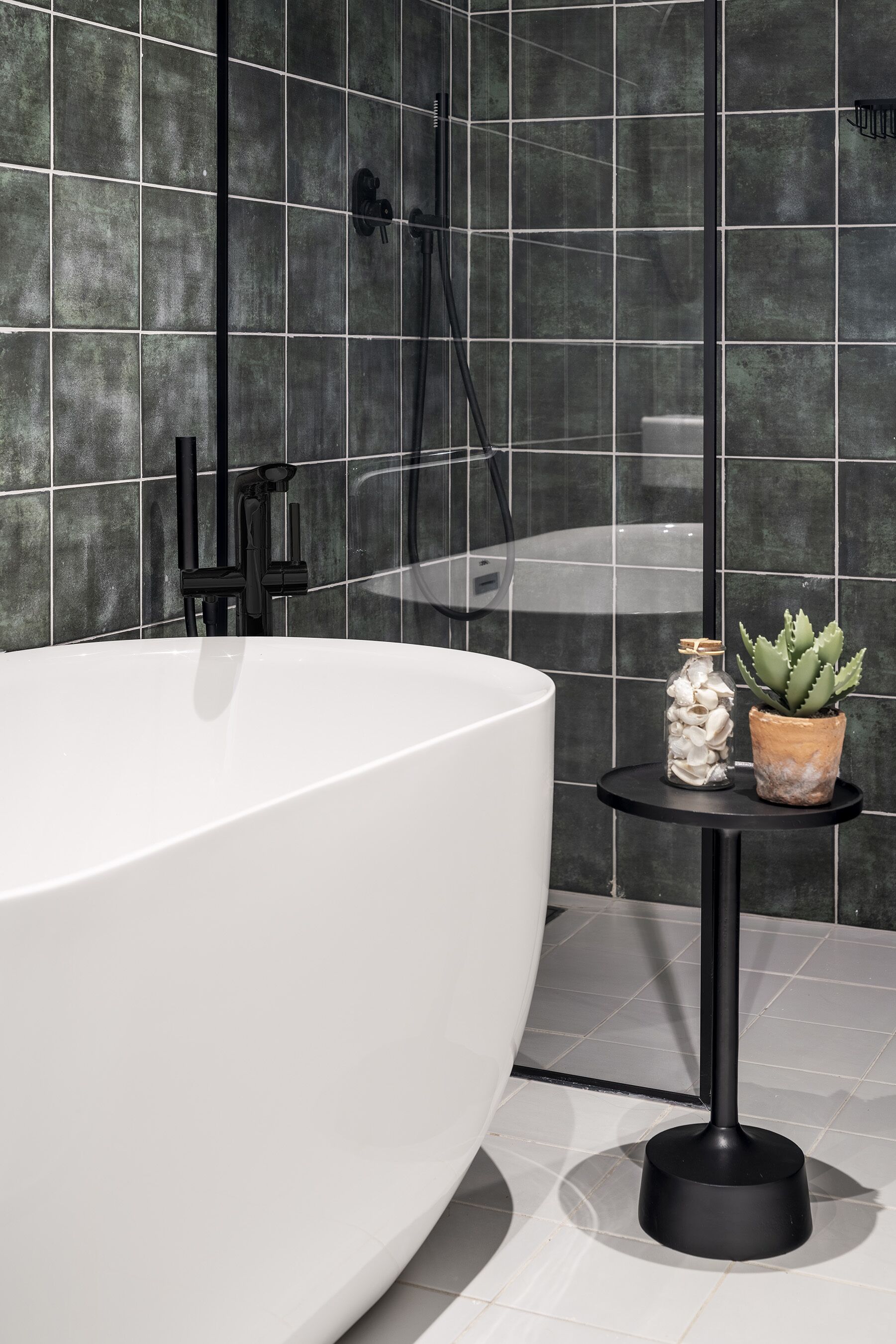 A modern bathroom with a large white bathtub, a black pedestal sink, and a small round table with decorative items.