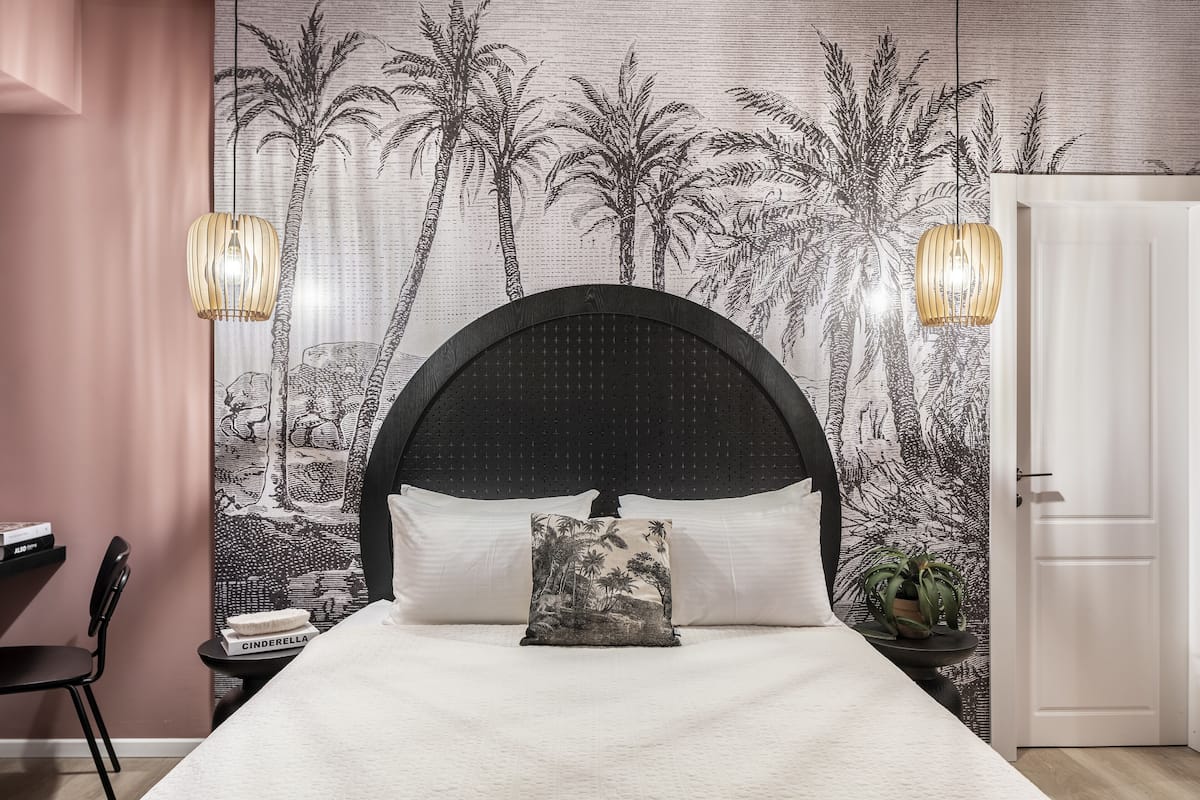 Une chambre à coucher comprenant un lit, une tête de lit, une table de chevet, une chaise, une bibliothèque et une porte.